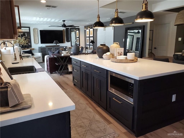 kitchen with pendant lighting, a center island, stainless steel microwave, and light hardwood / wood-style floors