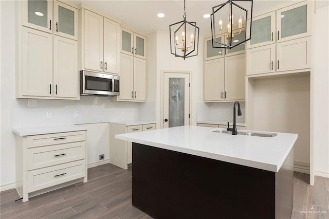 kitchen with stainless steel microwave, dark wood-type flooring, decorative light fixtures, a center island with sink, and a sink