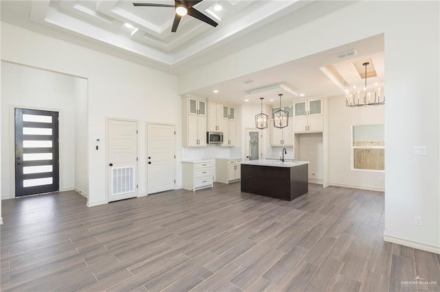 kitchen with visible vents, dark wood finished floors, a kitchen island with sink, a towering ceiling, and stainless steel microwave