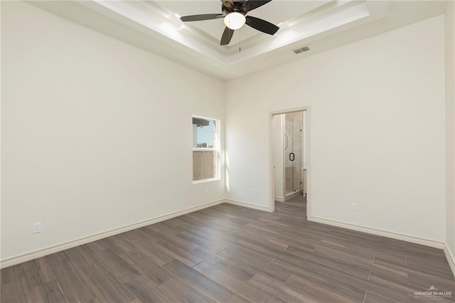 spare room with visible vents, dark wood-type flooring, ceiling fan, baseboards, and a raised ceiling