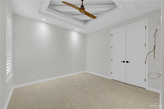 unfurnished bedroom with ceiling fan, light tile patterned flooring, a raised ceiling, and a closet