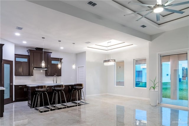 kitchen featuring dark brown cabinets, decorative light fixtures, a breakfast bar area, and an island with sink