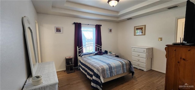 bedroom with a raised ceiling and dark hardwood / wood-style floors