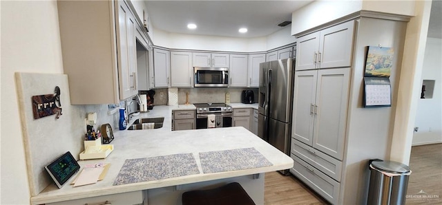 kitchen with sink, light wood-type flooring, tasteful backsplash, kitchen peninsula, and stainless steel appliances