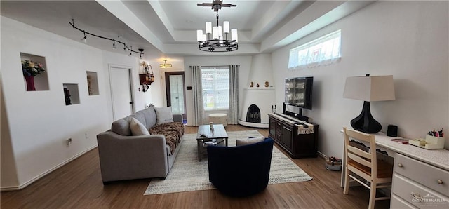 living room featuring an inviting chandelier, a tray ceiling, dark wood-type flooring, and rail lighting