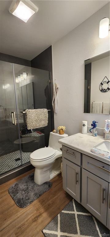 bathroom featuring wood-type flooring, walk in shower, vanity, and toilet