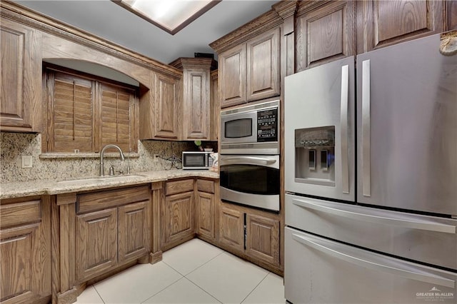 kitchen featuring sink, decorative backsplash, light stone countertops, appliances with stainless steel finishes, and light tile patterned flooring