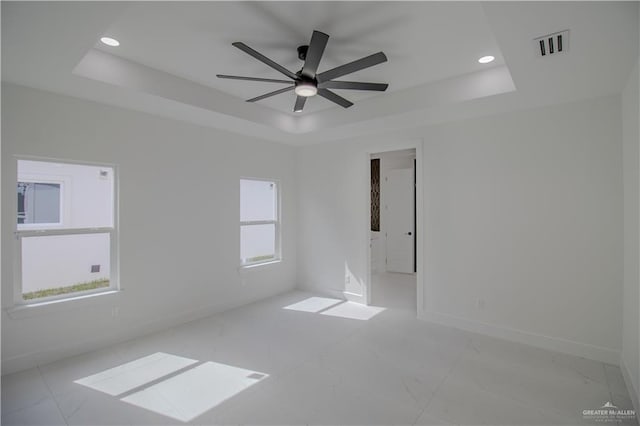 unfurnished room with a ceiling fan, marble finish floor, a tray ceiling, baseboards, and visible vents