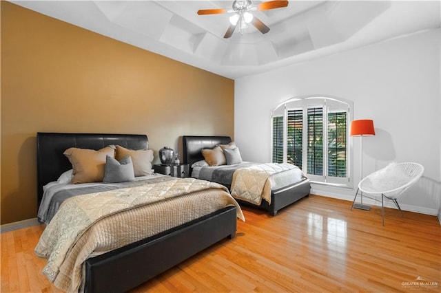 bedroom featuring a ceiling fan, a raised ceiling, light wood-style flooring, and baseboards