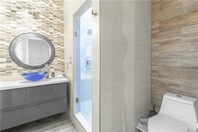 full bathroom with toilet, wood finished floors, vanity, a shower stall, and tile walls