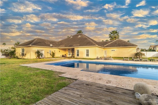 pool at dusk featuring an outdoor pool, a patio area, and a lawn