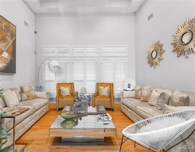 living area with a towering ceiling, visible vents, and wood finished floors