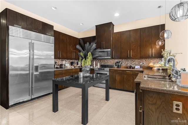 kitchen with a sink, stainless steel appliances, dark brown cabinets, pendant lighting, and backsplash