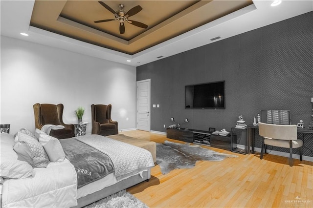 bedroom featuring an accent wall, a tray ceiling, wood finished floors, and baseboards