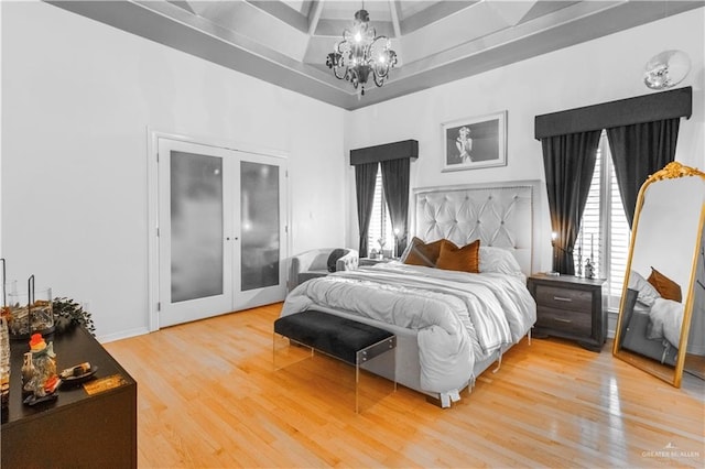 bedroom with a chandelier, a raised ceiling, wood finished floors, and french doors