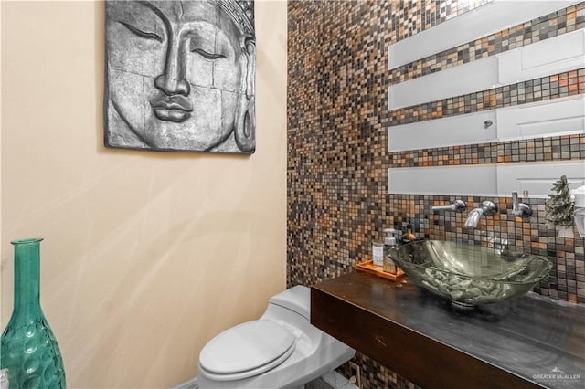 half bath featuring toilet, a sink, and decorative backsplash