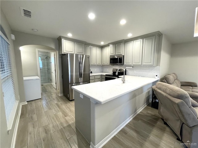 kitchen with sink, stainless steel appliances, tasteful backsplash, light hardwood / wood-style flooring, and kitchen peninsula