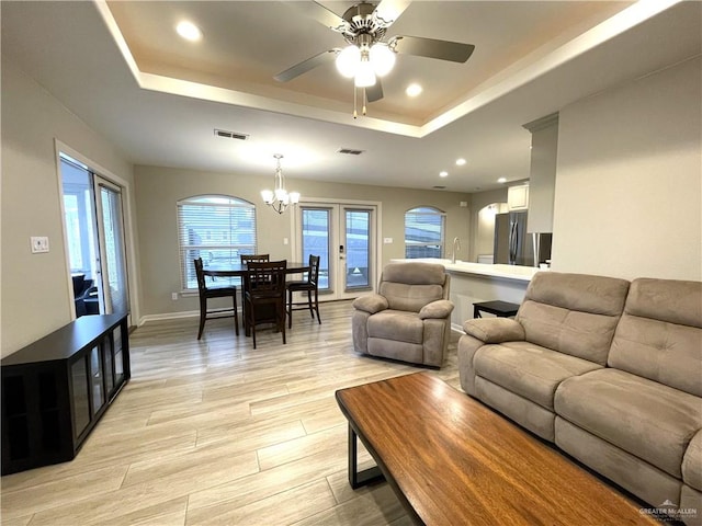 living room with french doors, ceiling fan with notable chandelier, a raised ceiling, sink, and light hardwood / wood-style floors