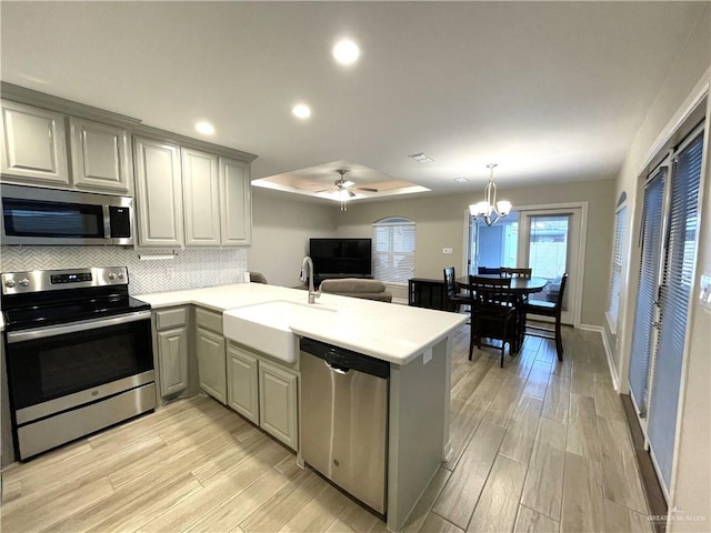 kitchen featuring kitchen peninsula, decorative backsplash, stainless steel appliances, sink, and light hardwood / wood-style flooring