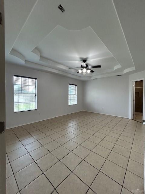 spare room with baseboards, a ceiling fan, a raised ceiling, and light tile patterned floors