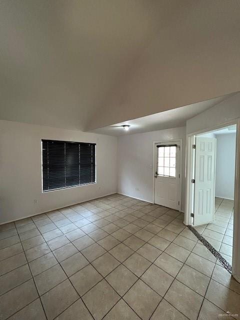 empty room with light tile patterned floors and lofted ceiling