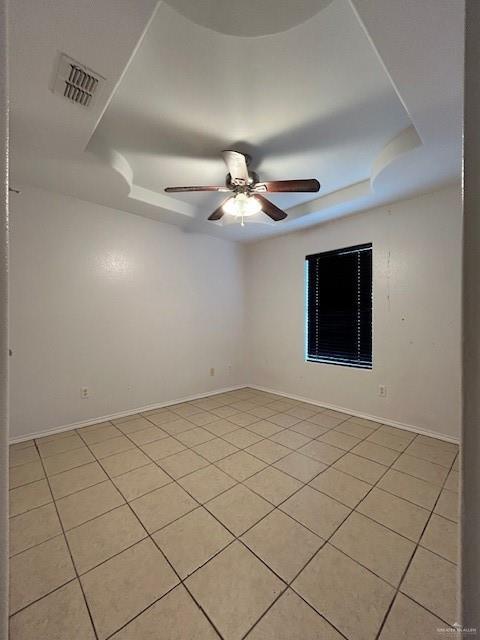 unfurnished room with visible vents, baseboards, ceiling fan, a tray ceiling, and light tile patterned floors