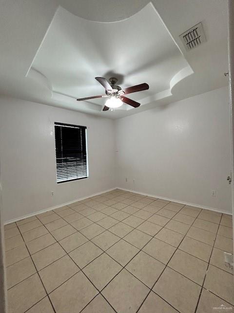 unfurnished room featuring visible vents, a ceiling fan, a raised ceiling, and light tile patterned floors
