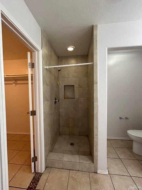 bathroom featuring a walk in closet, tile patterned flooring, a shower stall, and toilet