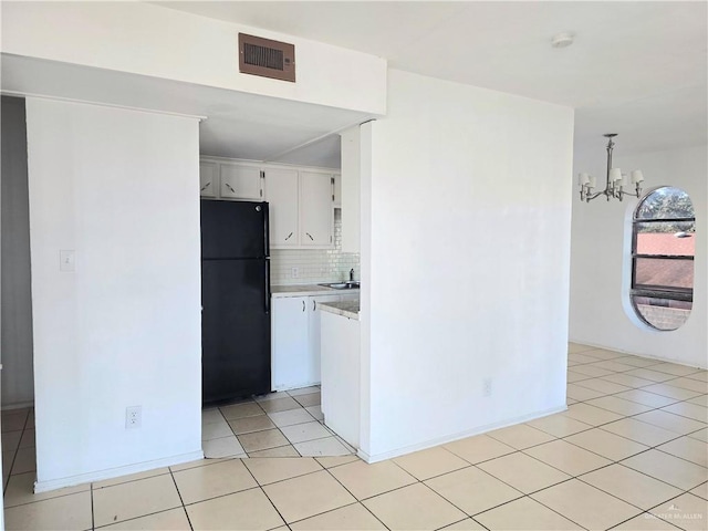 kitchen featuring pendant lighting, white cabinets, black fridge, decorative backsplash, and a notable chandelier