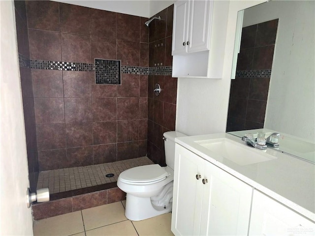 bathroom featuring tile patterned flooring, a tile shower, vanity, and toilet