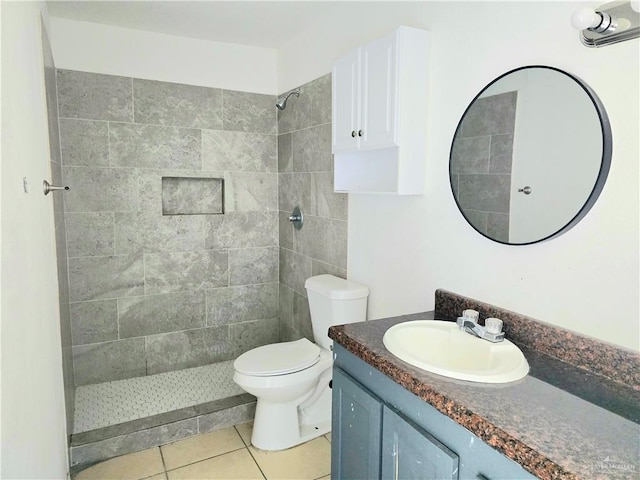 bathroom featuring tile patterned flooring, a tile shower, vanity, and toilet