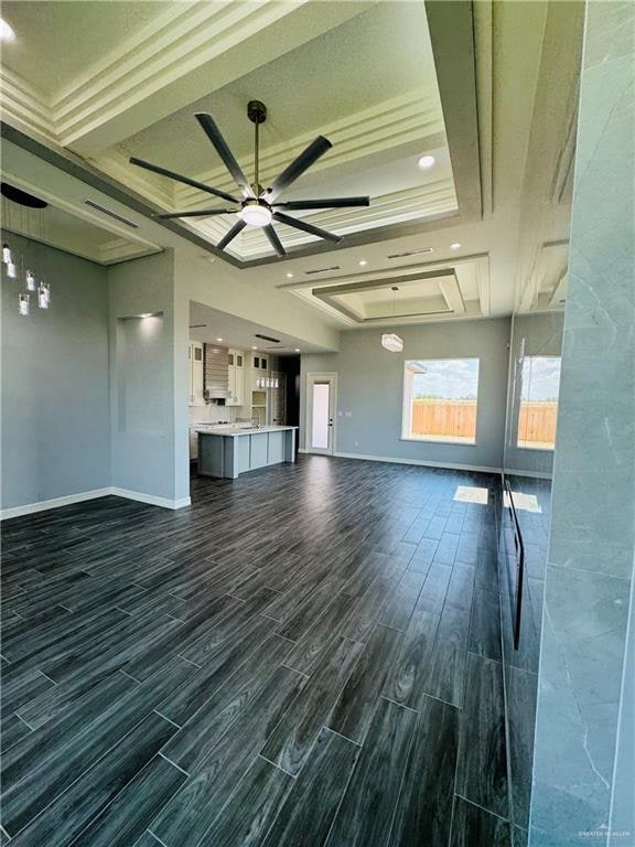 unfurnished living room featuring a raised ceiling, ceiling fan, dark hardwood / wood-style flooring, and ornamental molding