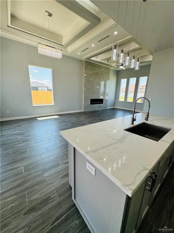 kitchen featuring pendant lighting, a center island with sink, light stone countertops, and sink