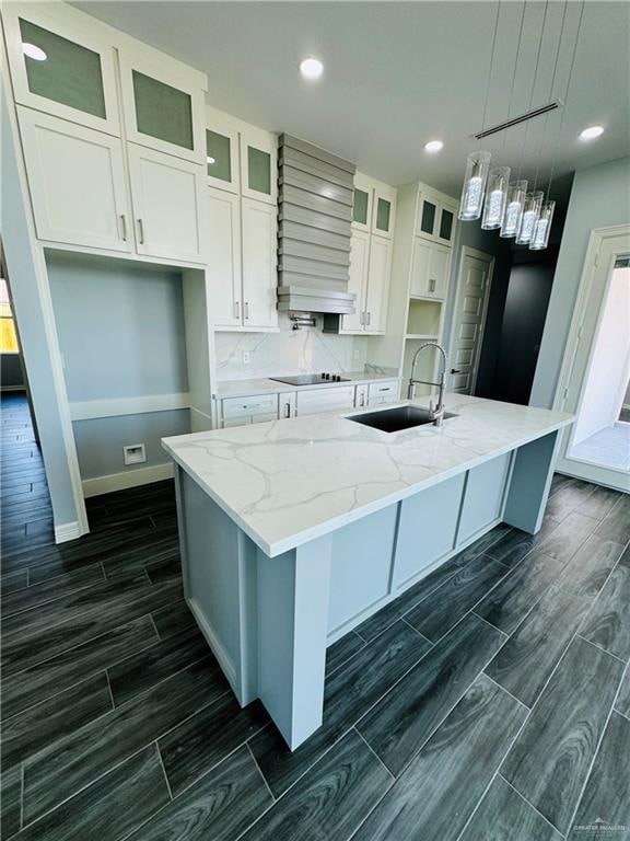 kitchen with light stone countertops, sink, decorative light fixtures, a center island with sink, and white cabinets