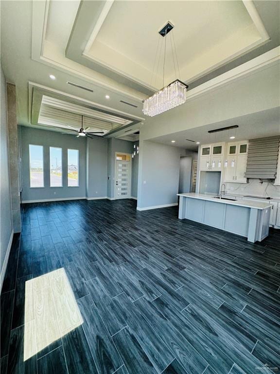 unfurnished living room with a raised ceiling, sink, dark wood-type flooring, and ceiling fan with notable chandelier