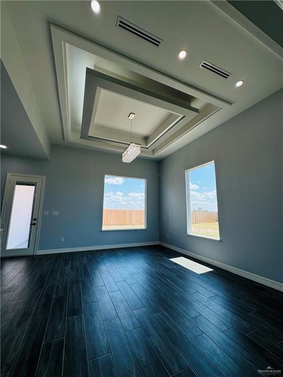 empty room featuring dark hardwood / wood-style floors, a tray ceiling, and a chandelier