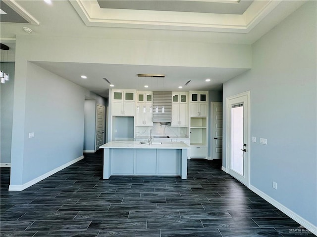 kitchen with decorative backsplash, a kitchen island with sink, and white cabinets