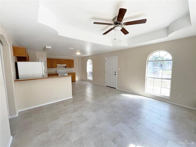 unfurnished living room featuring a raised ceiling and ceiling fan