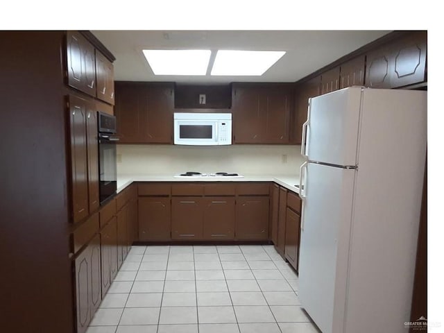 kitchen featuring a skylight, white appliances, light tile patterned floors, and dark brown cabinets