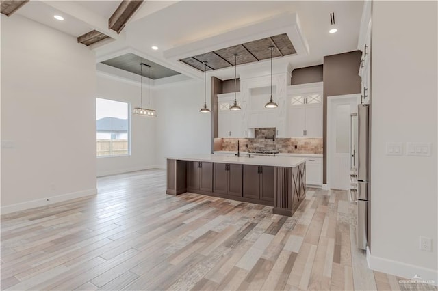 kitchen featuring a center island with sink, light countertops, tasteful backsplash, a sink, and coffered ceiling