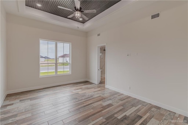 unfurnished room with a raised ceiling, light wood-style flooring, a ceiling fan, baseboards, and visible vents