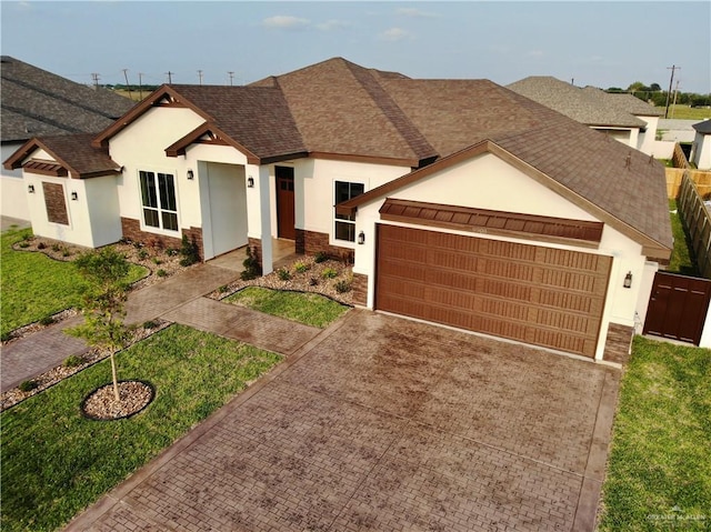 ranch-style home featuring driveway, roof with shingles, an attached garage, stone siding, and stucco siding