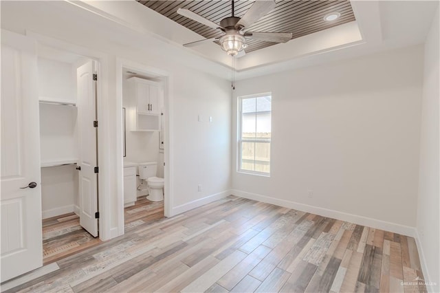unfurnished bedroom with a raised ceiling, baseboards, a closet, light wood finished floors, and a spacious closet