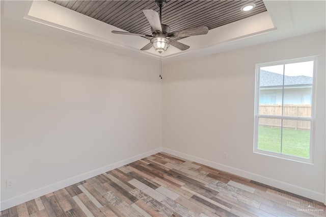 spare room featuring baseboards, a raised ceiling, ceiling fan, and light wood-type flooring