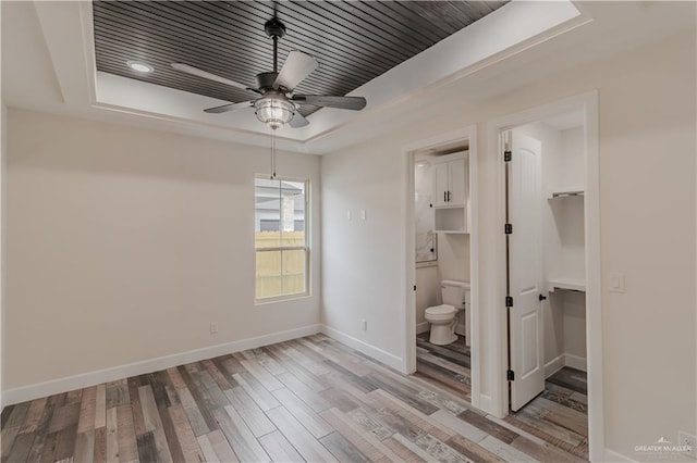 unfurnished bedroom with baseboards, a raised ceiling, ensuite bathroom, and wood finished floors
