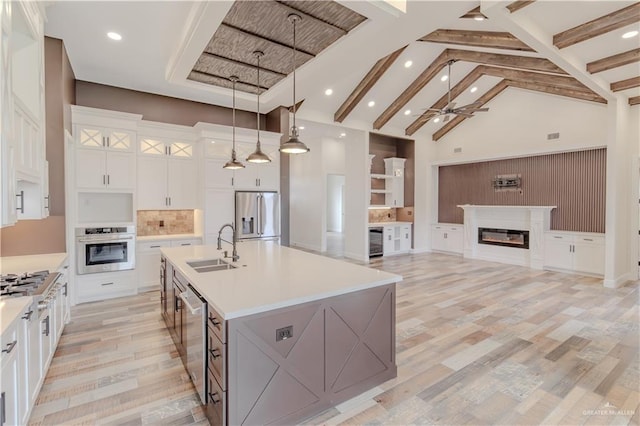kitchen featuring ceiling fan, a sink, high vaulted ceiling, a glass covered fireplace, and stainless steel appliances