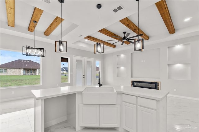 kitchen with ceiling fan, sink, beam ceiling, white cabinets, and a kitchen island