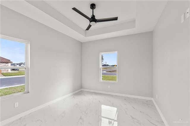 unfurnished room with a raised ceiling, ceiling fan, and plenty of natural light