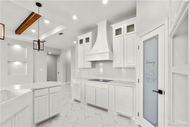 kitchen with hanging light fixtures, beamed ceiling, black electric stovetop, white cabinets, and custom range hood