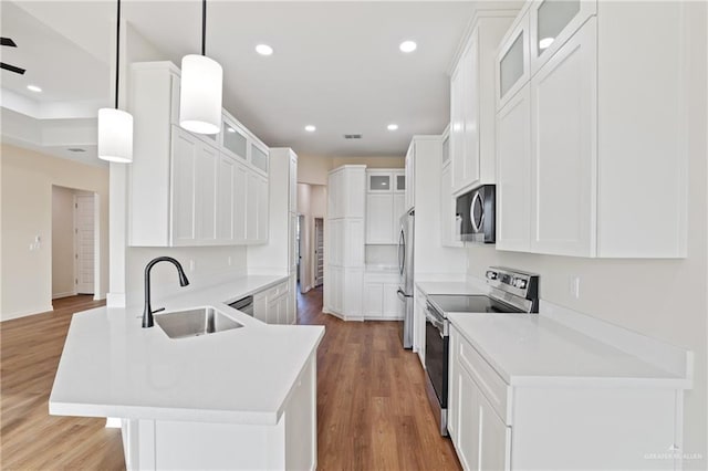 kitchen with stainless steel appliances, a peninsula, a sink, and light wood-style flooring